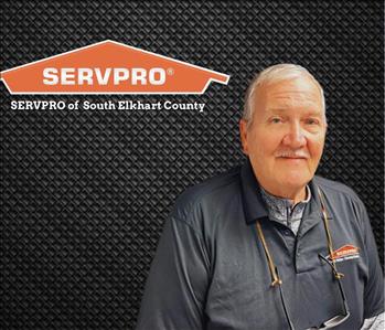 Man looking at camera in a black shirt on a black background with a SERVPRO logo on there wall